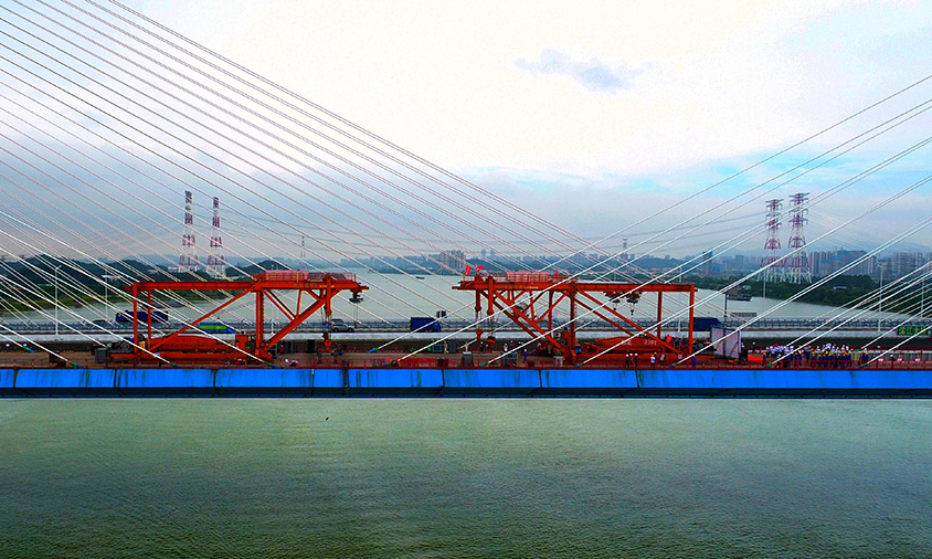 西江特大橋在橋梁建設史上實現了“三個首次”：為適應鐵路活載大的特點，首次在鐵路斜拉橋索塔錨固區采用新型鋼錨梁技術；首次在鐵路斜拉橋上采用復合不銹鋼橋面板；同時，為解決水源保護區鋼箱梁排水問題，首次采用具有排水功能的新型正交異性橋面板結構。圖為合龍現場。（金偉 攝）