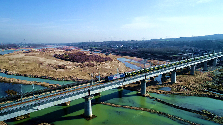 在隧道施工中，中鐵十四局建設者采用超前水平鉆排水和水壓爆破法施工，提高了單循環爆破進尺，確保了施工進度。在全線唯一一座轉體橋洋縣漢江特大橋跨京昆高速轉體橋施工中，他們采用活性粉末混凝土球鉸等先進設備，提升了施工效率。圖為列車駛過中鐵十四局承建的洋縣漢江特大橋。（肖永順 攝）
