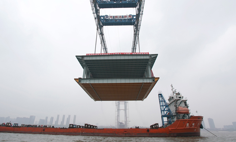 連通武漢三鎮中武昌與漢陽的楊泗港長江大橋，由中鐵大橋局承建，是武漢在建的第十座長江大橋，也是長江上首座雙層公路大橋。大橋主跨達1700米，一跨過長江，創造了雙層懸索橋跨度新紀錄。圖為11月15日，纜載吊機在吊裝重達1000噸的鋼梁。（新華社記者 程敏 攝）