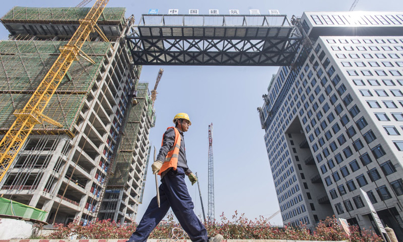 3月28日，經過48小時的走走停停，總重1500噸、高9.9米、寬18米、跨度76.5米的鋼結構連廊整體提升至離地73.6米的高空，橫亙于武漢光谷新城核心區域“中建·光谷之星”項目兩棟塔樓之間。圖為中建三局的建設者從提升完成的“空中生態綠廊”周邊走過。（新華社記者 肖藝九 攝）