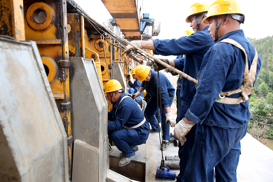 落梁吊裝過程需要40分鐘，精準對位時間占了一半。裝吊工分工協(xié)作，拿著水平尺測量支座平整度，用吊錘評估支座和中心、墩臺的錯動量，用鋼尺測量四角高差……每道工序都不能少，嚴謹?shù)墓ぷ鲬B(tài)度才能確保每一榀箱梁精準吊裝到位。圖為作業(yè)人員為架橋機過孔做準備工作。（黃詩偉 攝）