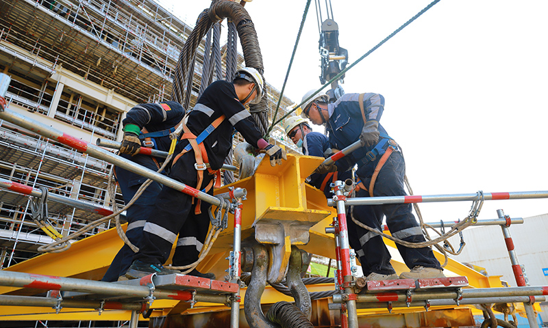 為有效緩解這一局面，高效推動(dòng)項(xiàng)目施工進(jìn)度，建造事業(yè)部青島公司在提升精細(xì)化管理能力和水平上下功夫。通過成立甲板片臨時(shí)倒運(yùn)小組，提前疏通車道障礙，讓原本滯緩的場地運(yùn)輸工作高效運(yùn)轉(zhuǎn)。圖為Mini E-House（電氣間）吊裝作業(yè)人員合力安裝吊裝鎖具。