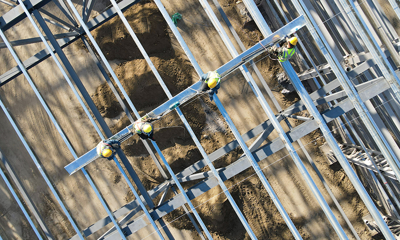 工人在20余米高的新疆塔城重點(diǎn)開(kāi)發(fā)開(kāi)放試驗(yàn)區(qū)一處風(fēng)機(jī)葉片制造項(xiàng)目頂部進(jìn)行屋面檁條安裝作業(yè)（5月18日無(wú)人機(jī)拍攝）。新華社記者 高晗 攝