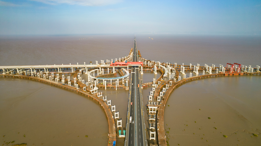 杭甬高速復線寧波一期工程全長55.833千米，為雙向六車道高速公路標準，設計時速120千米。該工程主線橋在寧波市鎮海區一跨直接越過甬舟高速金塘大橋，并設濱?；ネㄅc金塘大橋相接，主線橋箱梁梁底與金塘大橋橋面凈空約7.6米，海上架梁施工安全風險極高，為全線唯一一處Ⅳ級施工風險點。圖為濱?；ネㄖ骶€橋跨越金塘大橋架梁現場。