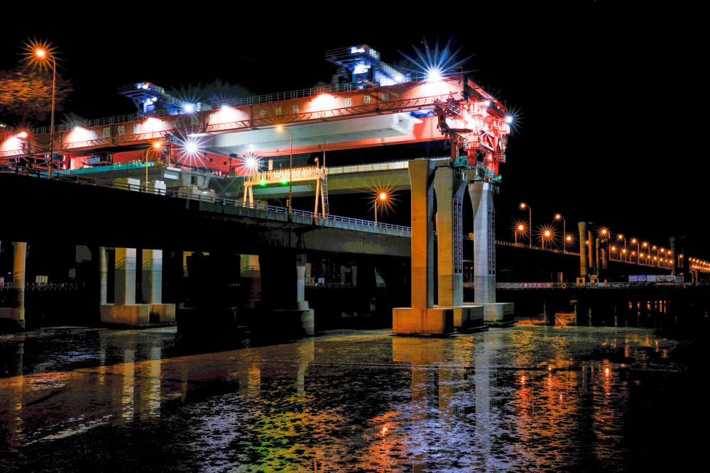 項目團隊圍繞海上50米大跨徑、1800噸超大噸位整孔預制箱梁運輸兩個方面開展科研攻關，研制了我國自主研發、目前世界上最大的公路架橋機“越海號”開展“梁上運架”施工，成功攻克箱梁單體重量大、超高橋面漸變橫坡、高低墩及1800米超小曲線半徑等技術難題，確保了箱梁架設和金塘大橋運營安全，創下了國內采用“梁上運架”技術單體最重的整孔預制箱梁施工紀錄。圖為跨金塘大橋架梁施工現場。