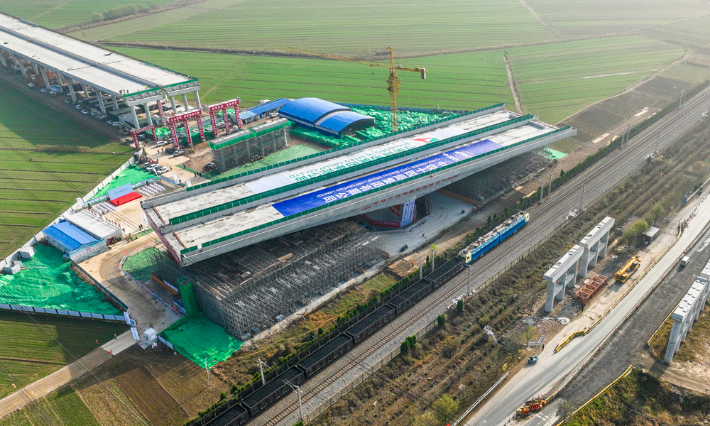 跨京滬鐵路轉(zhuǎn)體橋上部結(jié)構(gòu)采用預(yù)應(yīng)力混凝土T構(gòu)，跨徑組合為（68+68）米，下部結(jié)構(gòu)主墩采用“V”型空心墩設(shè)計，整幅橋梁全寬38.33米，轉(zhuǎn)體重量高達(dá)25680噸，主承臺深基坑開挖處臨近繁忙干線京滬鐵路，距路基坡腳線最近處僅有15米，臨近鐵路基坑開挖深度10余米，施工過程復(fù)雜、精度要求高。圖為轉(zhuǎn)體橋轉(zhuǎn)體中。