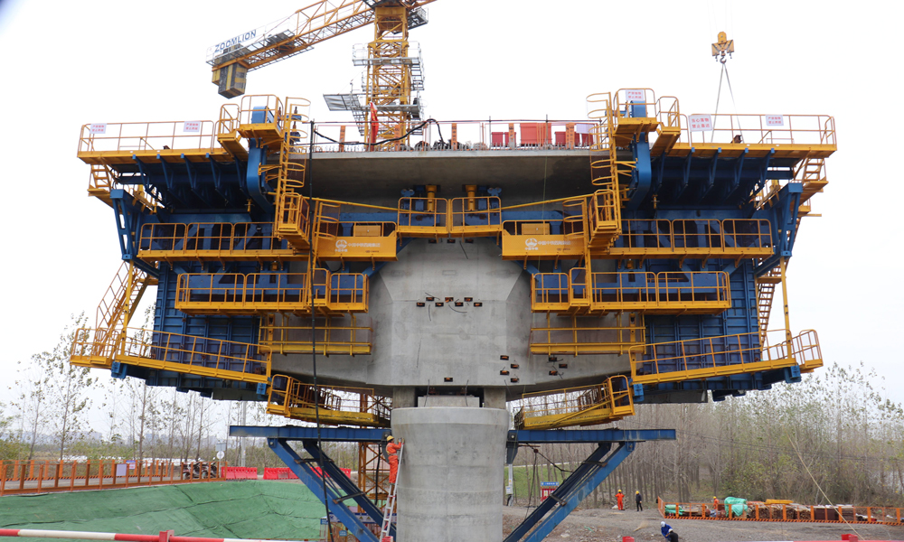 智慧造橋機由承重桿件、液壓整體模板、液壓調節、自動走行、信息化監控、鋼筋骨架整體吊裝、平臺防護等系統組成，并預留了智能蒸汽養護、自動噴淋等多功能系統安裝接口，集液壓傳動、智能操控、信息化監測技術于一體，極大解決了傳統掛籃在懸臂現澆連續梁施工中結構復雜、裝拆繁瑣等問題，大幅提高了懸臂現澆梁自動化、信息化和智能化建造水平，推廣前景廣闊。