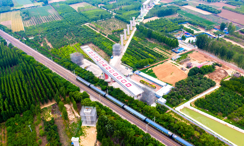 跨京九鐵路連續梁是雄安機場快線首座涉及運營鐵路的轉體梁，所跨京九鐵路每日運行列車多達百余列。為確保轉體期間京九鐵路安全運營，中鐵四局多次組織專家評審、優化施工方案，并在正式轉體前試轉，通過稱重平衡試驗測試轉體部分的不平衡力矩、偏心矩、摩阻力矩及摩擦系數等參數，以實現橋梁轉體的配重要求，在轉體過程中，根據轉臺上標識的轉角刻度及梁面軸線實行嚴格監控。圖為跨京九鐵路轉體梁轉體前航拍。