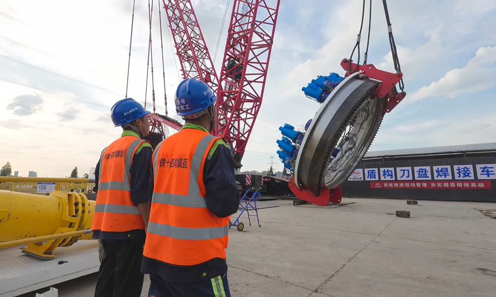 為確保10月底盾構始發(fā)這一重大節(jié)點，300多名施工人員在節(jié)日期間堅守崗位，奮戰(zhàn)在一線。該隧道全長6.379公里，采用“盾構+明挖”進行施工，其中盾構段長4.4公里。圖為施工人員為主驅動下井做準備。