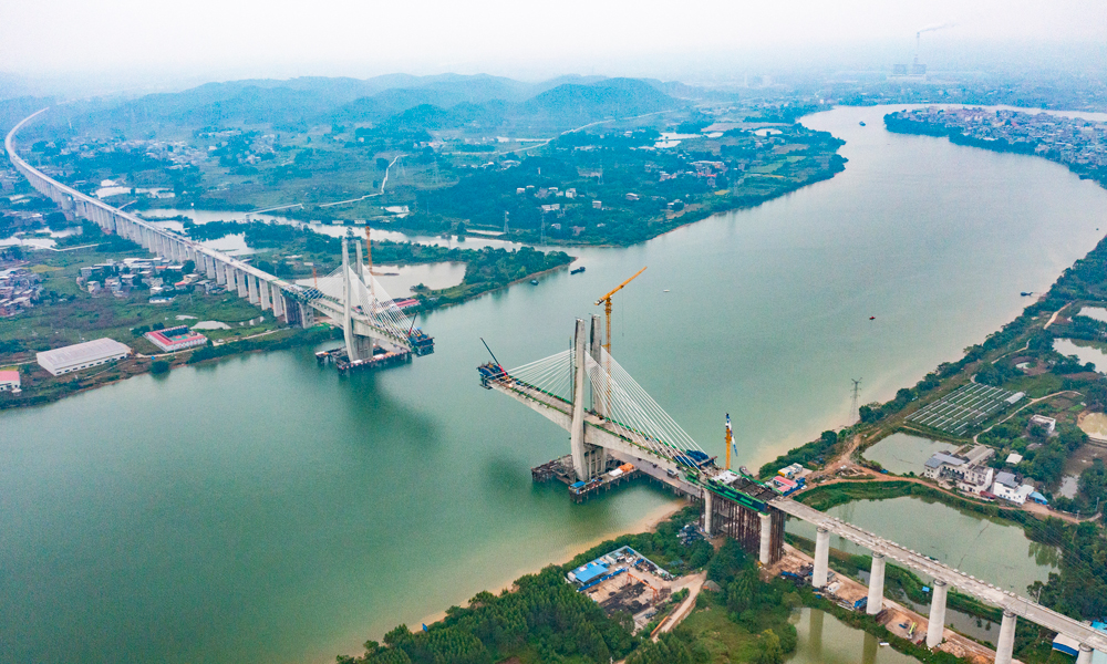 該特大橋鋼混結合段單側懸臂施工長15米，由2.7米長混凝土梁和12.3米鋼梁組成，懸灌重量為1800噸，由于鋼混段施工位于航道中間，需要采用懸吊施工工藝。建設團隊創新思路方法，將鋼梁分為4.65米和7.65米兩次吊裝，再進行混凝土分段澆筑的施工工藝，解決超長、超重鋼混段懸灌施工難題。圖為施工現場航拍中景。