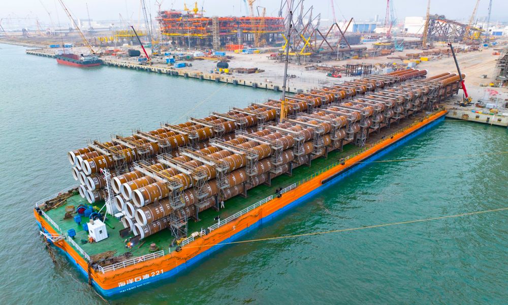 此次裝船作業(yè)采用SPMT（自行模塊運(yùn)輸車）滾裝方式，刷新“海洋石油221”船單側(cè)裝船重量紀(jì)錄。面對船舶調(diào)載、承重極限、潮水周期受限等挑戰(zhàn)，項目團(tuán)隊反復(fù)優(yōu)化作業(yè)方案，密切關(guān)注船舶與潮水狀況，全力確保裝船作業(yè)安全順利。圖為“?；枴睂?dǎo)管架鋼樁完成裝船。