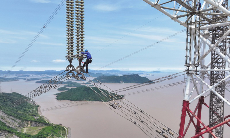 此次檢修規模大、技術難度高，洛春5495線、洛曉5496線為跨海輸電線路，連接兩條線路的兩座高370米的輸電鐵塔分別位于舟山大貓山和寧波涼帽山，兩座輸電鐵塔檔距達2756米。檢修人員登上位于大貓山的輸電鐵塔，在高低落差達280米、最低點距海面高度超84米的線路開展走線作業。圖為檢修人員通過絕緣子串下到跨海輸電導線上。