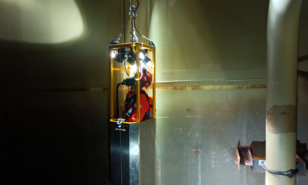 為了確保平臺凝析油艙處于良好運行狀態，掌握艙內設備運轉情況，平臺工作人員會定期開展清艙檢測作業。圖為“深海一號”現場作業人員搭乘空間極其狹小的特制工作吊籃進入凝析油艙內部進行檢查。周宇 攝