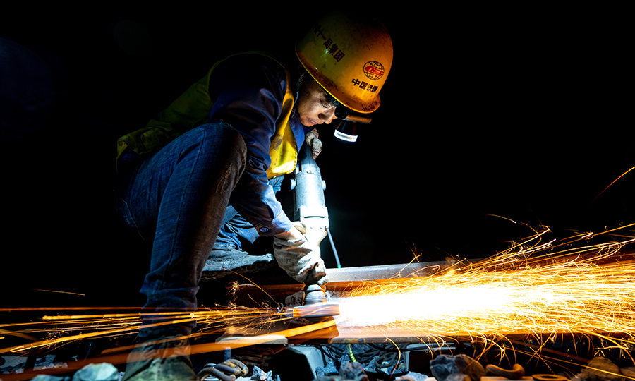 在400多公里的拉林鐵路線上，高寒缺氧、晝夜溫差大，如何保證全線無縫焊接的質量？有這樣一群夜行者，他們用晝伏夜出的工作方式給了我們答案。白天鋼軌溫度達到了60攝氏度，為保證“應力放散鎖定”工序的質量，他們通常晚上9點等軌溫降下來了才開始工作，為了不耽誤第二天施工運輸車輛的通行，凌晨5點就匆匆下班。他們手里握著的不僅僅是900攝氏度的鋼軌更是藏族同胞的信任與期盼。圖為工人正在進行除銹作業(yè)。（丁慶濱 攝）