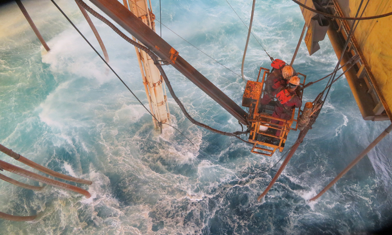 圖為“海洋石油982”鉆井平臺(tái)起防噴器作業(yè)中，員工在風(fēng)浪中懸掛拆除鵝頸管，確保平臺(tái)順利起航避臺(tái)。